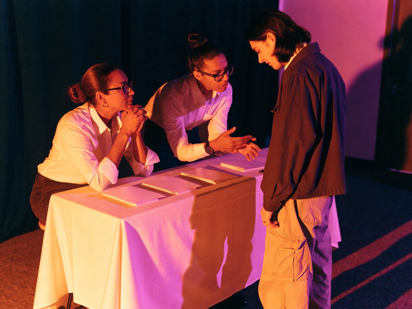 Two adult organizers welcome an adult visitor at an information table with plain leaflets