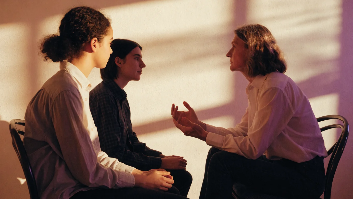 Two adult friends sit with an adult support professional in a calm room