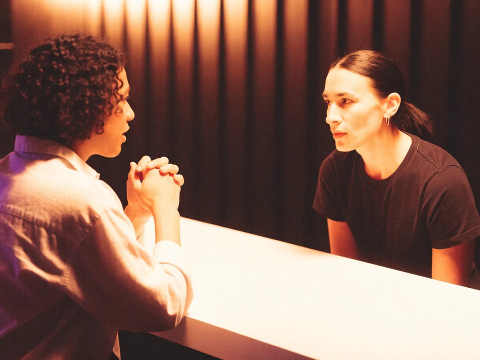 An adult guest speaks with an attentive staff member across a clear bar counter.